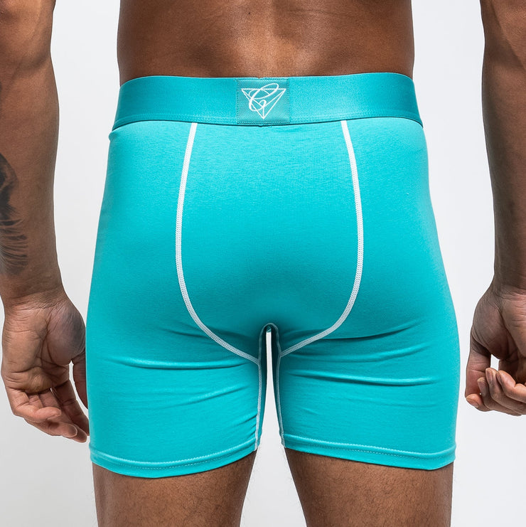 Tsunami SZN blue and white Chromatic briefs, styled with a fresh, ocean-inspired aesthetic. The icy blue waistband with bold branding contrasts against the clean white fabric, creating a crisp, wave-like vibe. He stands with relaxed confidence, water droplets on his skin catching the light to enhance the coastal energy of the look. The form-fitting cut and breathable material highlight comfort without sacrificing edge. This pair makes a splash clean, bold, and unapologetically eye-catching.