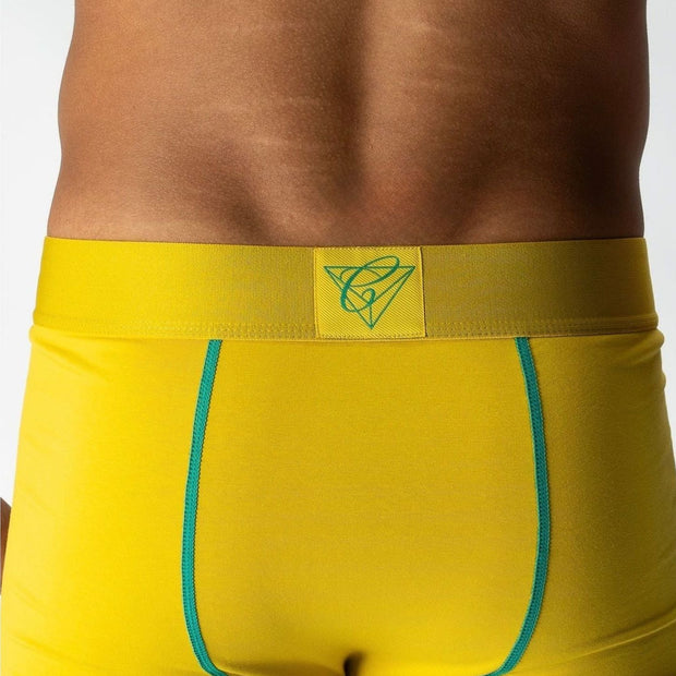 Chromaldinho models a vibrant yellow pair of Chromatic underwear, standing confidently with his torso slightly turned to highlight the bold branded waistband. The bright color pops against his skin tone, drawing attention to the clean lines and contoured fit of the briefs. His signature diamond chain rests on his chest, adding a flash of luxury to the bold, streetwear-inspired aesthetic. The lighting accentuates his physique while keeping the focus on the underwear’s sharp, flattering cut and energetic col