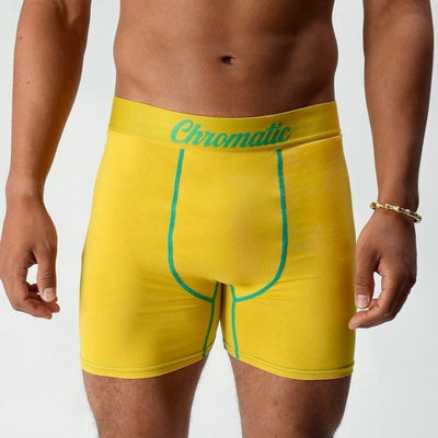 Chromalddinho models a vibrant yellow pair of Chromatic underwear, standing confidently with his torso slightly turned to highlight the bold branded waistband. The bright color pops against his skin tone, drawing attention to the clean lines and contoured fit of the briefs. His signature diamond chain rests on his chest, adding a flash of luxury to the bold, streetwear-inspired aesthetic. The lighting accentuates his physique while keeping the focus on the underwear’s sharp, flattering cut and energetic col