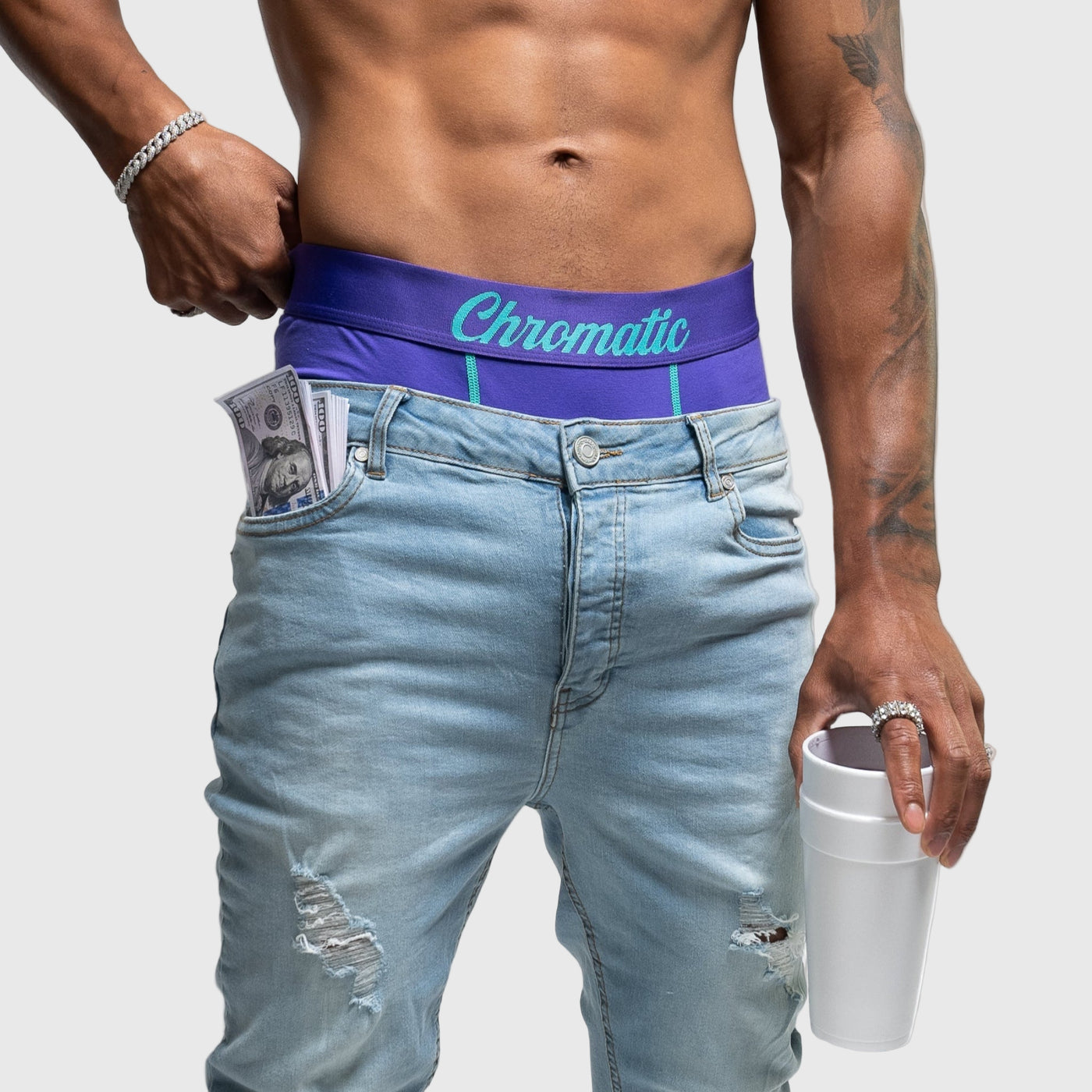 Man wearing a purple blue underwear with 'Chromatic' branding, holding a white styrofoam cup.