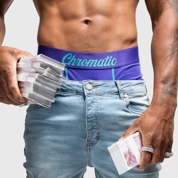 Person wearing a purple 'Chromatic' underwear and light blue jeans, holding money.