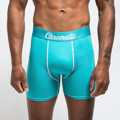 Tsunami SZN blue and white Chromatic briefs, styled with a fresh, ocean-inspired aesthetic. The icy blue waistband with bold branding contrasts against the clean white fabric, creating a crisp, wave-like vibe. He stands with relaxed confidence, water droplets on his skin catching the light to enhance the coastal energy of the look. The form-fitting cut and breathable material highlight comfort without sacrificing edge. This pair makes a splash clean, bold, and unapologetically eye-catching.