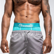 Tsunami SZN blue and white Chromatic briefs, styled with a fresh, ocean-inspired aesthetic. The icy blue waistband with bold branding contrasts against the clean white fabric, creating a crisp, wave-like vibe. He stands with relaxed confidence, water droplets on his skin catching the light to enhance the coastal energy of the look. The form-fitting cut and breathable material highlight comfort without sacrificing edge. This pair makes a splash clean, bold, and unapologetically eye-catching