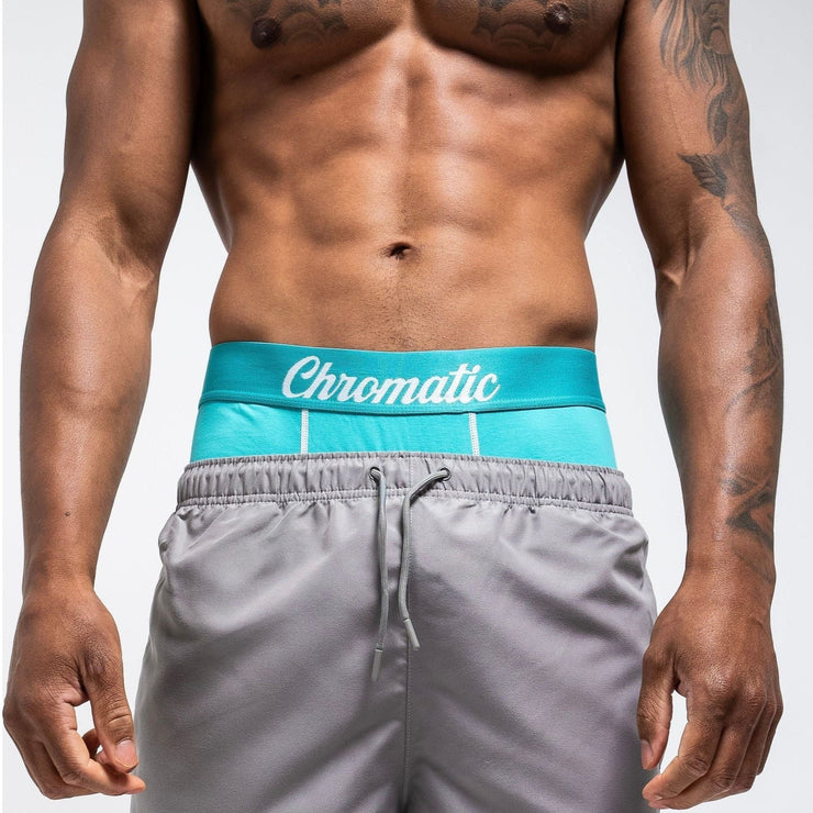 Tsunami SZN blue and white Chromatic briefs, styled with a fresh, ocean-inspired aesthetic. The icy blue waistband with bold branding contrasts against the clean white fabric, creating a crisp, wave-like vibe. He stands with relaxed confidence, water droplets on his skin catching the light to enhance the coastal energy of the look. The form-fitting cut and breathable material highlight comfort without sacrificing edge. This pair makes a splash clean, bold, and unapologetically eye-catching