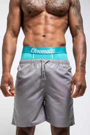 Man wearing grey swim shorts with a blue waistband featuring 'Chromatic' branding on a white background.